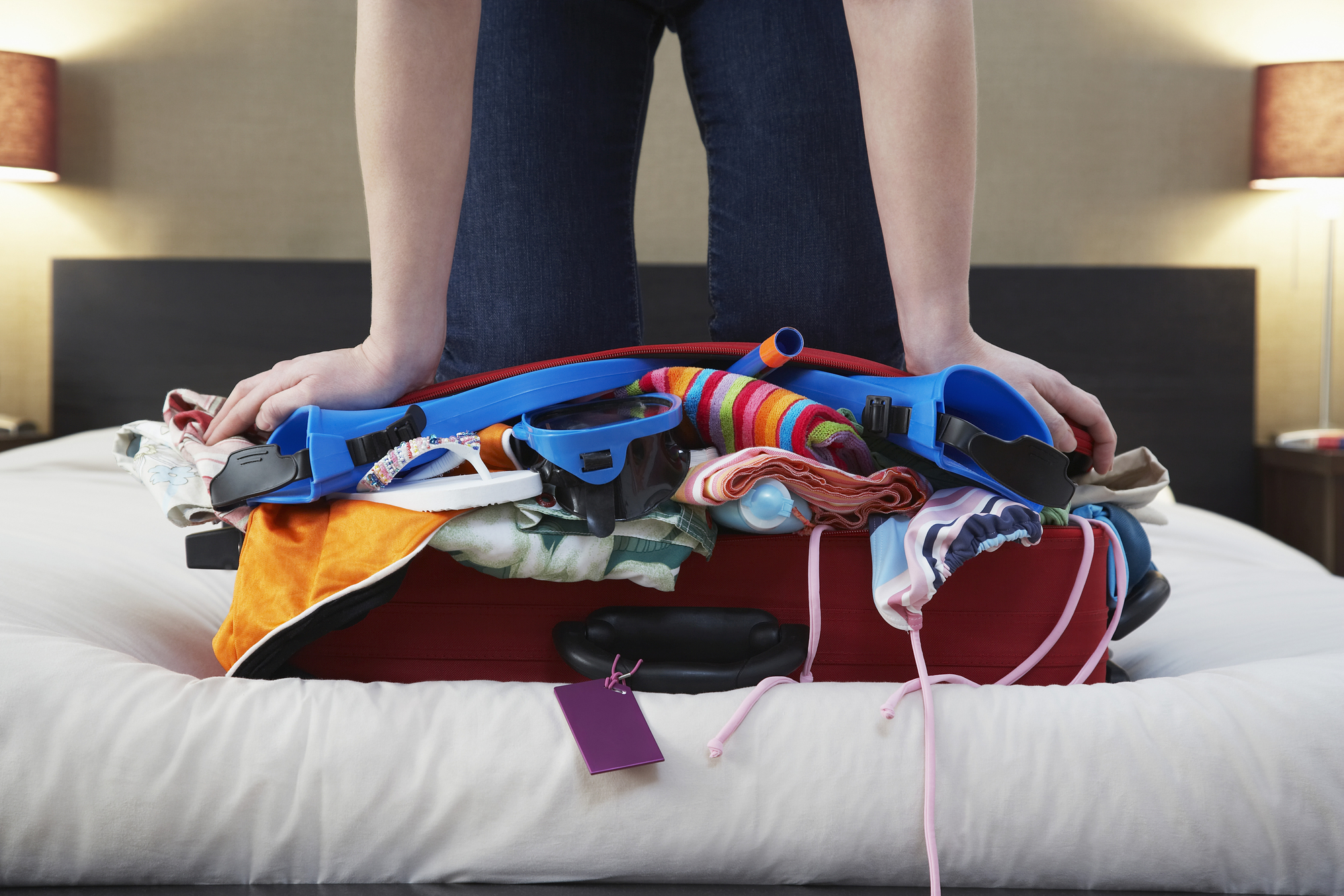 Woman kneeling on overstuffed suitcase